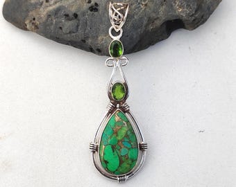 May include: A silver pendant with a teardrop-shaped green stone, accented with smaller green stones. The pendant has a detailed silver design and is set against a dark gray rock. The text "925 Silver Legacy" is at the bottom.
