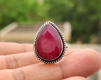 Peut inclure: Bague en argent ornée d'un grand rubis en forme de poire. Le rubis est d'un rouge profond et est serti dans un sertissage à lunette avec un motif de corde torsadée sur le bord. Le texte "925 Silver Legacy" est en bas.