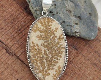 May include: Oval pendant with a silver bail and a natural stone center. The stone features a beige background with brown, fern-like patterns. The pendant is set in a silver beaded frame. The text "925 Silver Legacy" is visible.