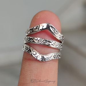 Puede incluir: Primer plano de tres anillos de plata con diseños florales y de hojas. Los anillos están apilados, creando un efecto de capas. Los anillos están en un dedo. El texto "925 Silver Legacy" está en la parte inferior.