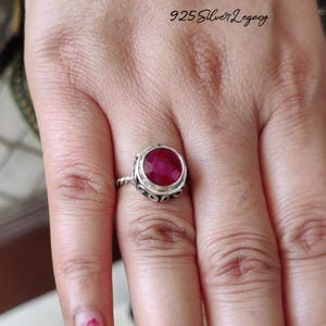 May include: A sterling silver ring featuring a large, oval-cut ruby gemstone. The ring has an ornate, detailed setting with a twisted band. The text "925 Silver Legacy" is visible in the upper right corner.