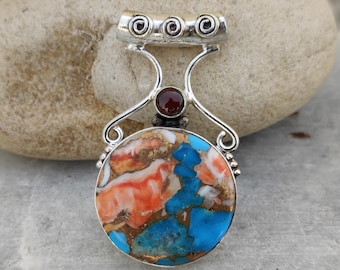 May include: A silver pendant with a round, colorful stone featuring orange, blue, and gold hues. The pendant has a silver bail with three spiral designs and a small, round, red gemstone. The bottom of the pendant has the text "925 Silver Ligy".