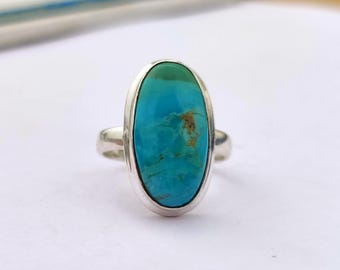 May include: A silver ring with a large oval turquoise gemstone. The turquoise is a vibrant blue-green color with brown markings.