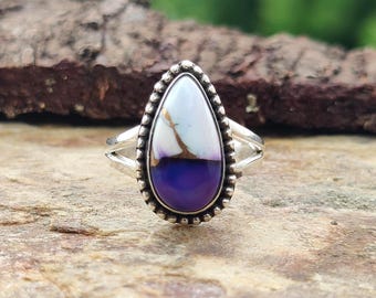 May include: A sterling silver ring featuring a teardrop-shaped stone. The stone is divided into white, gold, and deep purple sections, framed by a beaded silver border. The ring's band has a split design. The text "925 Silver Legacy" is at the bottom.