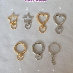 Op de afbeelding: Assortiment sleutelhangers in goud- en zilverkleuren, met ster- en hartvormen en ronde sluitingen. De afbeelding bevat de tekst "Keychains you can add."
