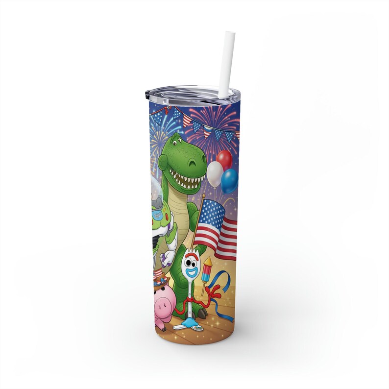 May include: A tall, insulated tumbler with a colorful design featuring characters from the Toy Story movie. The design includes a green dinosaur, a pig, and other characters, along with American flags and fireworks. The tumbler has a silver lid and a white straw.