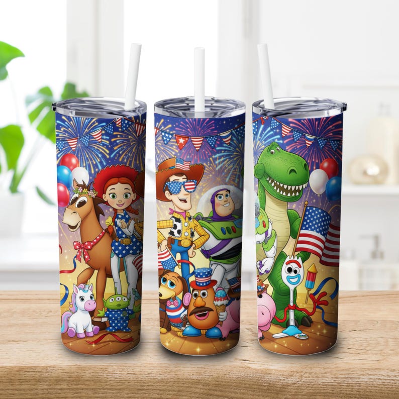 May include: Three stainless steel tumblers with white straws, featuring a patriotic design with characters from the Toy Story movie. The design includes fireworks, flags, and balloons, with a wooden table in the foreground.