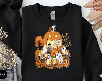 Könnte beinhalten: Schwarzes Sweatshirt mit einem Halloween-Motiv. Das Design zeigt einen großen Kürbis, Snoopy, Charlie Brown, Lucy und andere Peanuts-Charaktere. Der Schriftzug "Welcome Great Pumpkin" befindet sich auf einem Schild.
