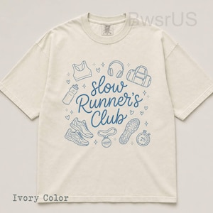 May include: Ivory-colored t-shirt with a blue graphic that reads "Slow Runner's Club." The design includes illustrations of running shoes, a sports bra, headphones, a water bottle, a gym bag, a medal, and a stopwatch.