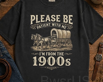 May include: Black t-shirt with a vintage illustration of a horse-drawn covered wagon. The shirt features the text "PLEASE BE PATIENT WITH ME I'M FROM THE 1900s" in a decorative font. The shirt is made of a soft, comfortable material.