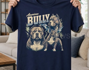 May include: A navy blue short-sleeve t-shirt featuring a graphic print of three American Bully dogs. The text "American BULLY" is printed in a bold, light-colored font above the dogs, which are surrounded by stylized lightning bolt illustrations.