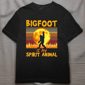 May include: Black t-shirt with a Bigfoot graphic. The design features a silhouette of Bigfoot in front of a full moon, with the text "BIGFOOT is my SPIRIT ANIMAL" in yellow and white.