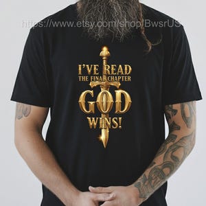 May include: Black t-shirt with a gold-colored sword design and the text "I'VE READ THE FINAL CHAPTER GOD WINS!". The design is centered on the front of the shirt.