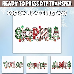 May include: A white DTF transfer featuring the name "SOPHIA" in a festive Christmas design. The letters are decorated with Christmas trees, candy canes, and other holiday elements. Additional transfers show the names "TAYLOR", "CUSTOM", and "JAMES". The text "READY TO PRESS DTF TRANSFER" is at the top.