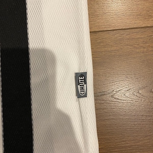 May include: White athletic jersey with a black vertical stripe on the left side. The jersey has a mesh texture and a small tag that reads "CLIMALITE". The jersey is made of a lightweight, breathable material.