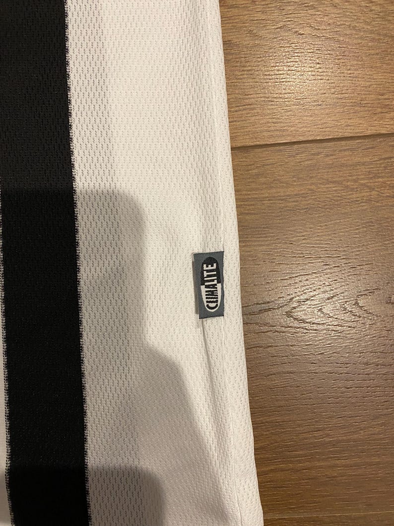 May include: White athletic jersey with a black vertical stripe on the left side. The jersey has a mesh texture and a small tag that reads "CLIMALITE". The jersey is made of a lightweight, breathable material.