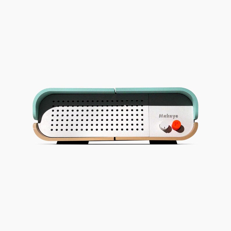 May include: A rectangular, modern-style speaker with a light teal top and a wooden base. The speaker has a white front with small black holes and the word "Makeye" printed on the side. An orange button is visible.