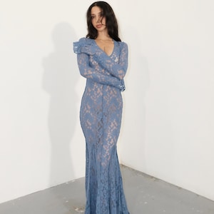 May include: A floor-length, long-sleeved dress crafted from blue lace fabric. The garment features a deep V-neckline and a fitted silhouette that flares slightly at the hem, showcasing a detailed floral lace pattern throughout the entire piece.