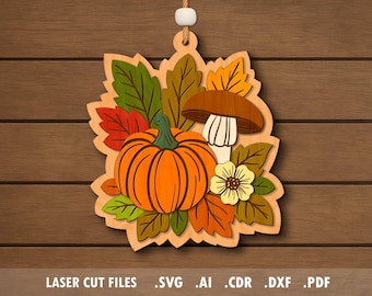 Op de afbeelding: Houten herfstdecoratie met een oranje pompoen, paddenstoel en bladeren in groen, rood en geel. Een kleine gele bloem is ook inbegrepen. De decoratie hangt aan een wit touwtje. De onderkant van de afbeelding heeft de tekst: LASER CUT FILES .SVG .AI .CDR .DXF .PDF.