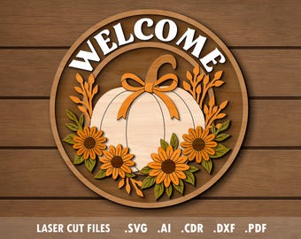 Op de afbeelding: Houten ronde bord met het woord "WELCOME" in het wit. Het bord toont een pompoen met een oranje strik, omringd door oranje bladeren en zonnebloemen. Het bord staat op een houten achtergrond.