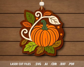 May include: Wooden fall-themed decoration featuring a layered design of a pumpkin, leaves, and decorative swirls. The pumpkin is orange with a green stem, surrounded by green, orange, and white leaves. The design hangs from a white string.