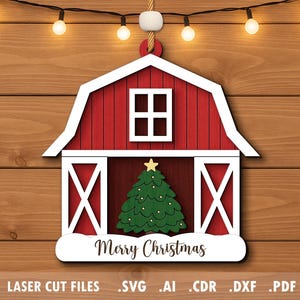 May include: A wooden Christmas ornament shaped like a red barn with white trim. The barn features a green Christmas tree with a gold star and the words "Merry Christmas". The ornament is hanging against a wooden background with string lights.