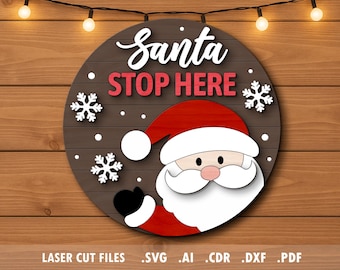 May include: A round wooden sign with a Santa Claus design. The sign features the words "Santa STOP HERE" in white and red, along with snowflakes. The Santa illustration has a red hat and suit, white beard, and black gloves. The sign is on a wooden background.