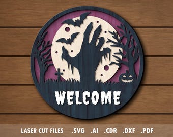 May include: A round, layered wooden Halloween sign with a spooky design. The sign features a zombie hand reaching towards a full moon, bats, trees, and a pumpkin. The word "WELCOME" is displayed at the bottom.