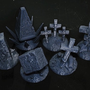 Puede incluir: Colección de decoraciones de cementerio en miniatura, grises y desgastadas. El conjunto incluye varias formas, como cruces, obeliscos y estructuras geométricas, todas con intrincados detalles tallados. Los artículos están dispuestos sobre una superficie oscura.