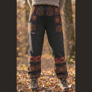 Puede incluir: Pantalones grises oscuros con detalles estampados en rojo, dorado y marrón. Los pantalones tienen una cintura estampada, bolsillos y detalles en la parte inferior de las piernas. Se usan con botas de senderismo, ideales para actividades al aire libre.