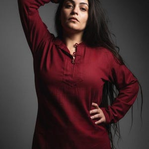 May include: A long-sleeved burgundy shirt with a button-up neckline and a small pocket. The shirt is made of a soft material and is a solid colour. The model is wearing the shirt.