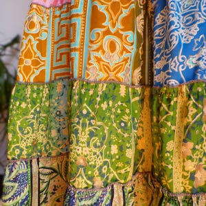 Pu&ograve; includere: Una gonna patchwork con un design a strati. La gonna presenta una variet&agrave; di tessuti fantasia nei toni del rosa, oro, blu, verde e turchese. I tessuti hanno disegni floreali e geometrici. La gonna ha un orlo a balze e un bordo decorativo.