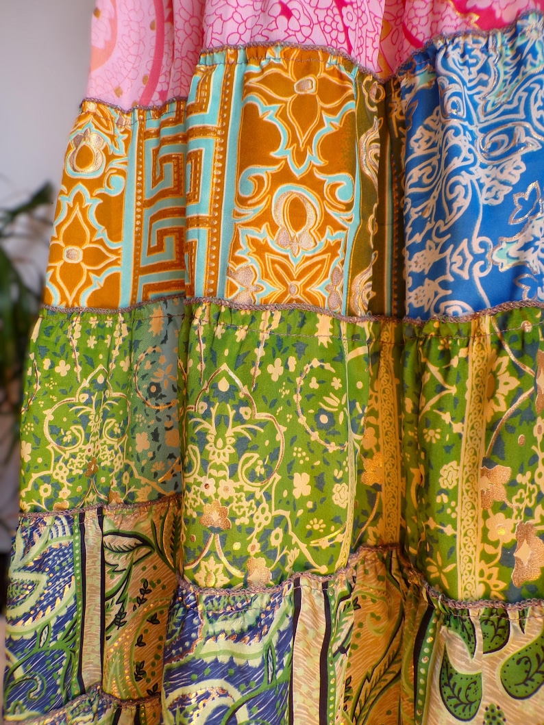 Pu&ograve; includere: Una gonna patchwork con un design a strati. La gonna presenta una variet&agrave; di tessuti fantasia nei toni del rosa, oro, blu, verde e turchese. I tessuti hanno disegni floreali e geometrici. La gonna ha un orlo a balze e un bordo decorativo.