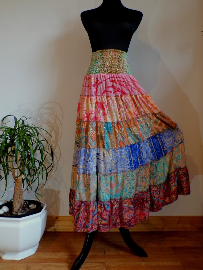 Pu&ograve; includere: Una gonna lunga a pi&ugrave; strati con un colorato design patchwork. La gonna presenta un'ampia fascia elastica in vita e una silhouette fluida. Il tessuto mostra una variet&agrave; di motivi e colori, tra cui rosa, blu, arancione e verde. La gonna &egrave; esposta su un manichino nero.