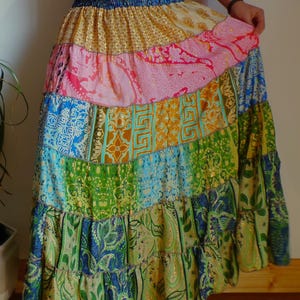 Pu&ograve; includere: Una gonna lunga a balze con elastico blu in vita e design patchwork. La gonna presenta pannelli di vari colori e motivi, tra cui rosa, oro, verde e blu, creando uno stile boh&eacute;mien.