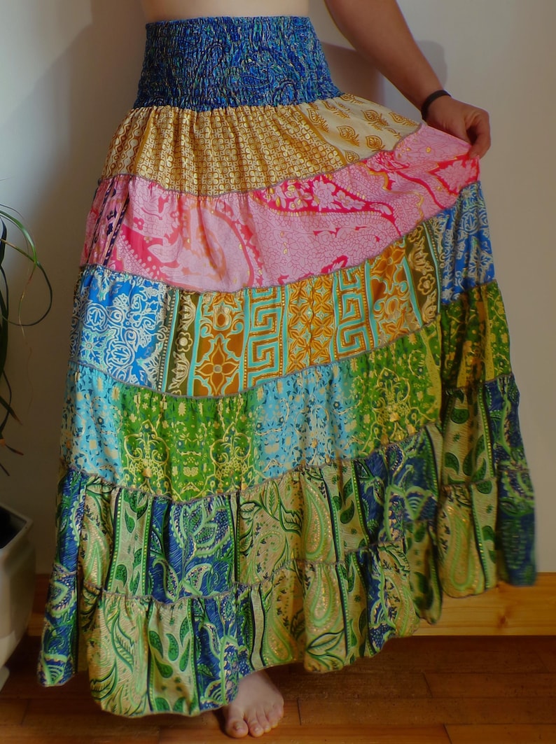 Pu&ograve; includere: Una gonna lunga a balze con elastico blu in vita e design patchwork. La gonna presenta pannelli di vari colori e motivi, tra cui rosa, oro, verde e blu, creando uno stile boh&eacute;mien.