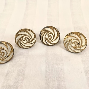 May include: Four vintage, round buttons with a white swirl design and gold-colored trim. The buttons are arranged on a striped, off-white fabric background. Each button has a diameter of approximately 1 inch.