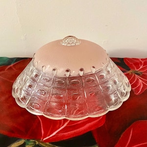 May include: A vintage glass lampshade with a pink, frosted top and a clear, textured bottom. The bottom section has a grid-like pattern with oval details. The lampshade is a light fixture.