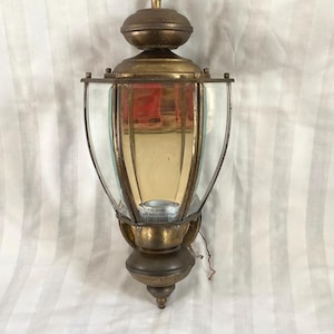 May include: Vintage brass outdoor wall-mounted lantern with clear glass panels. The lantern has a decorative top and bottom, with a bulb visible inside. The fixture has a classic design, suitable for exterior lighting.