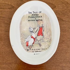 Puede incluir: Plato ovalado de cerámica con una escena de "The Tale of Jemima Puddle-Duck" de Beatrix Potter. La ilustración muestra un pato y un zorro en un bosque, con texto.