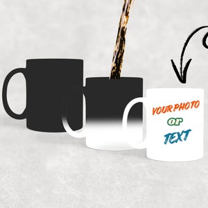 Może przedstawiać: Trzy białe ceramiczne kubki, jeden czarny, jeden przechodzący z czarnego na biały i jeden biały z napisem "YOUR PHOTO OR TEXT" w kolorze pomarańczowym, zielonym i niebieskim. Ciemny płyn jest wlewany do środkowego kubka.