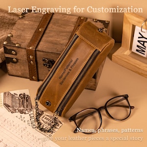 Può includere: Un astuccio in pelle marrone con cerniera, catena e la scritta "Name/Patterns/ Sentences & Phrases". L'astuccio è accanto a una scatola di legno, occhiali e la scritta "Names, phrases, patterns give your leather pieces a special story."