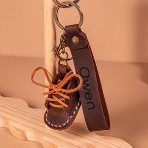 Pode incluir: Um porta-chaves de couro castanho escuro com um pendente de bota em miniatura com atacadores castanhos claros e uma tira de couro a condizer gravada com o nome Owen. O porta-chaves inclui um anel de metal e um fecho mosquetão.