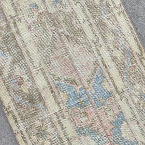 May include: A rectangular, vintage rug with a distressed look. It has a cream background with vertical stripes and floral patterns in blue, pink, and brown. The rug's design suggests it is a decorative floor covering, suitable for a home.