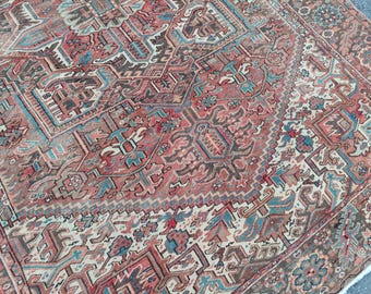 Puede incluir: Una alfombra tejida con un complejo patrón geométrico en tonos terracota, rosa viejo, azul cerceta y crema. El diseño incluye intrincados motivos florales, bordes angulares y formas simétricas distribuidas por toda la superficie.