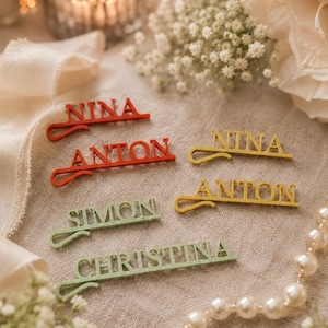 Könnte beinhalten: Mehrfarbige Namensschilder mit verschiedenen Namen in einer serifenlosen Schriftart. Die Namen sind "NINA", "ANTON", "SIMON" und "CHRISTINA". Die Karten sind rot, gelb und grün und für Hochzeiten oder Veranstaltungen gedacht.