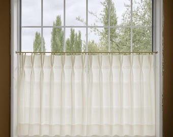 May include: A window with a white frame and a grid pattern, showcasing a view of trees and a cloudy sky. Cream-colored, pleated curtains hang from a gold-toned rod, adding a touch of elegance to the window's design. The curtains are made of a light, semi-sheer fabric.