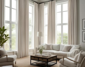 May include: A living room with large windows and white curtains. A white sofa with cushions sits in front of the windows. A coffee table with a black metal frame and a wooden top sits in front of the sofa. A white armchair with a throw pillow sits to the right of the sofa. A floor lamp with a white shade sits in the corner of the room.