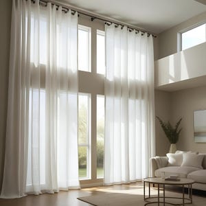 May include: Long, sheer white curtains hang from a dark rod, draping in front of large windows. The curtains create a soft, airy feel. The room has a neutral colour palette with a sofa, coffee table, and a vase of greenery.