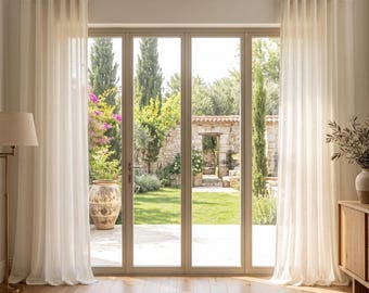 May include: Floor-to-ceiling off-white curtains hang from a silver metal rod with rings, framing a large glass door. The sheer fabric drapes in vertical folds, covering the sides of the doorway while allowing light to pass through the panels.